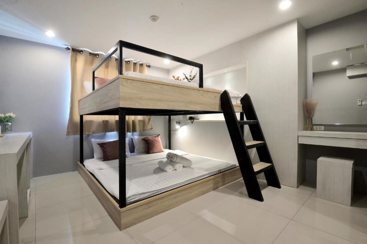 Un lit superposé avec un bureau et une chaise, une échelle et une petite table de chevet avec une lampe.