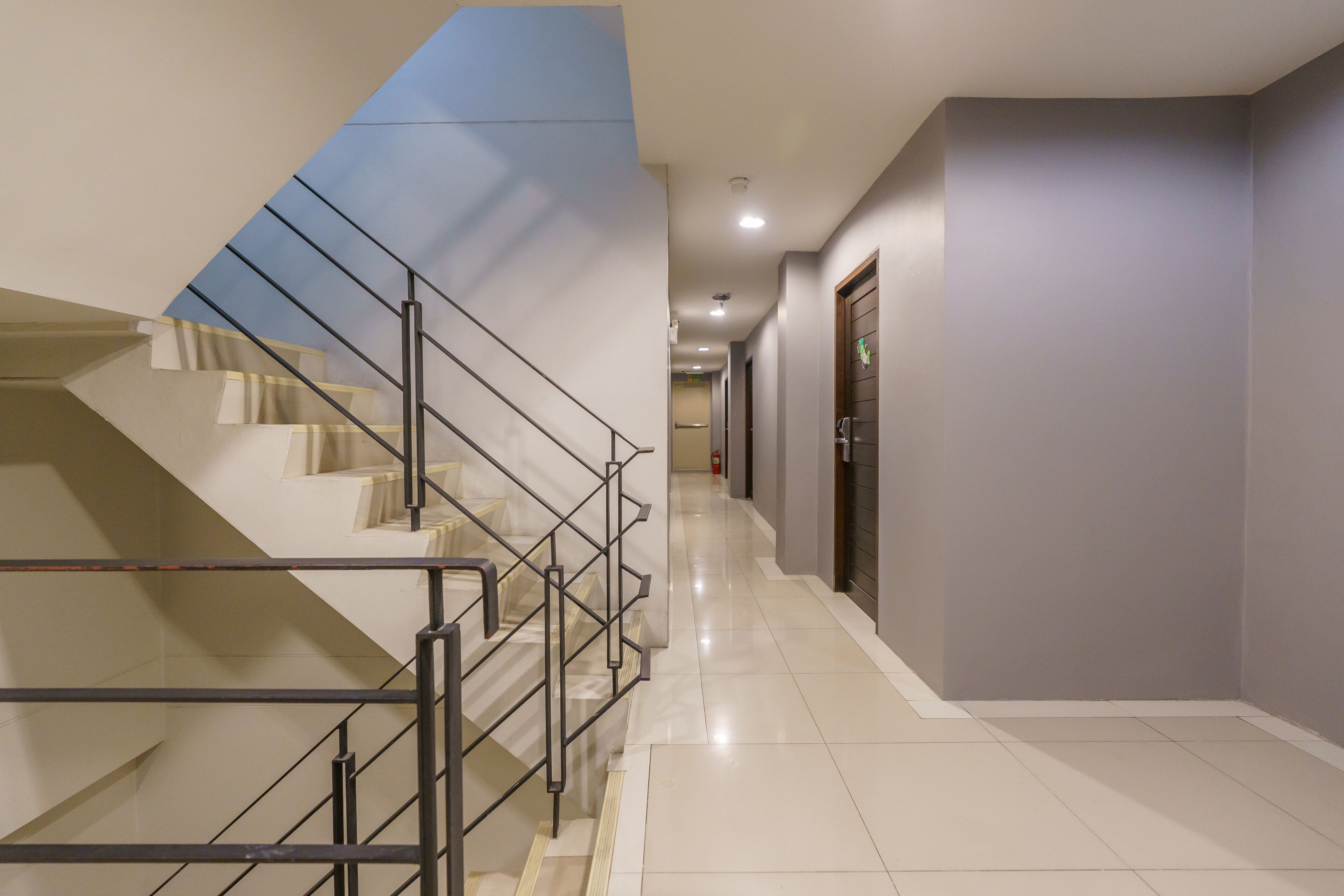 A modern hotel corridor with a staircase, a fire extinguisher, and a door at the end.
