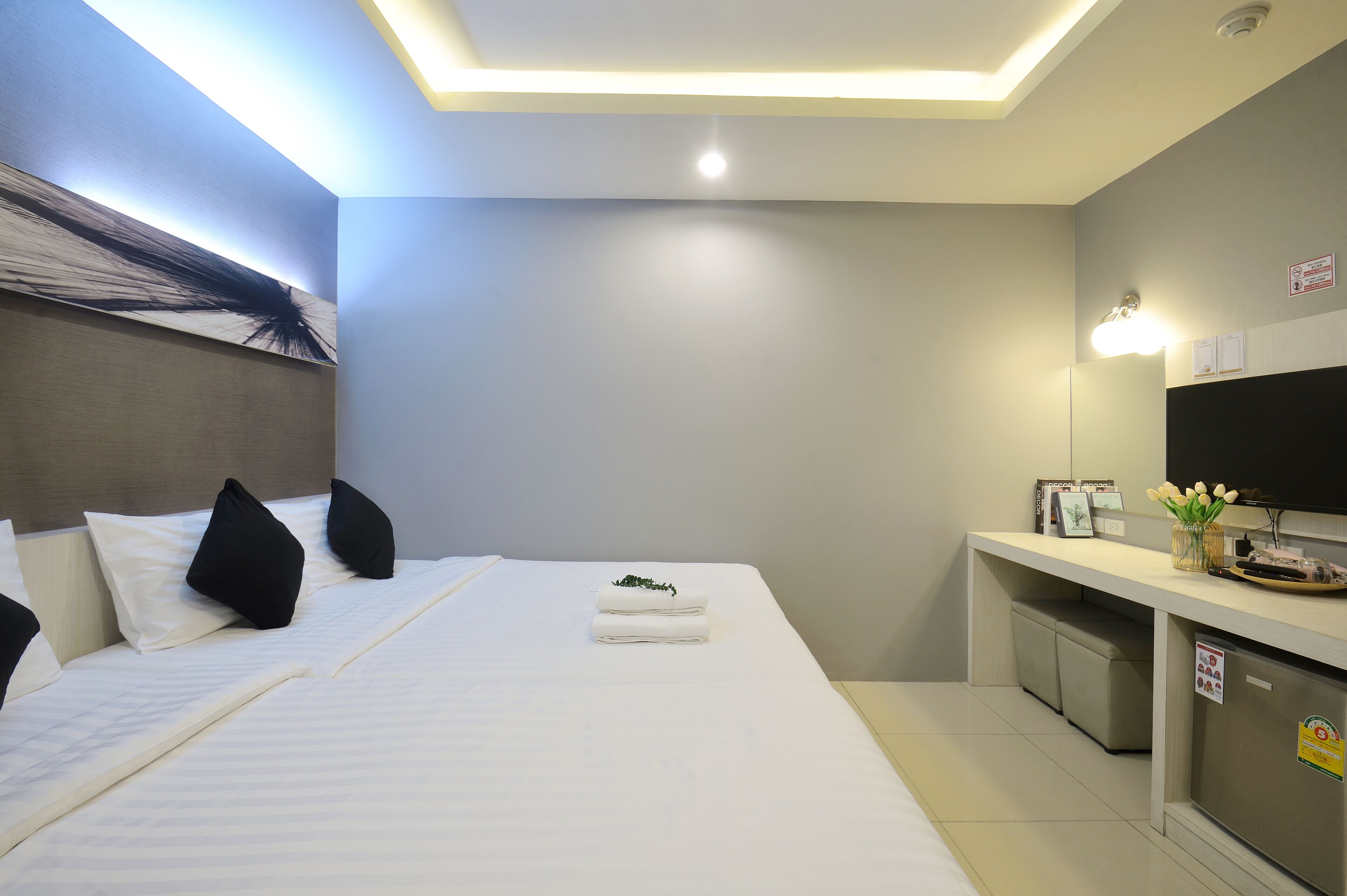 Une chambre d’hôtel équipée d’un lit, d’oreillers, d’un bureau avec un téléviseur à écran plat, d’un petit réfrigérateur et d’une lampe fixée au mur.
