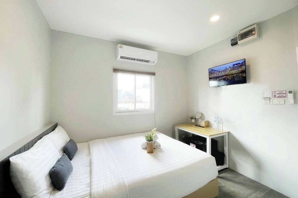 Une chambre d’hôtel avec un lit, une petite table de chevet agrémentée d’une plante, un téléviseur fixé au mur et un appareil de climatisation.