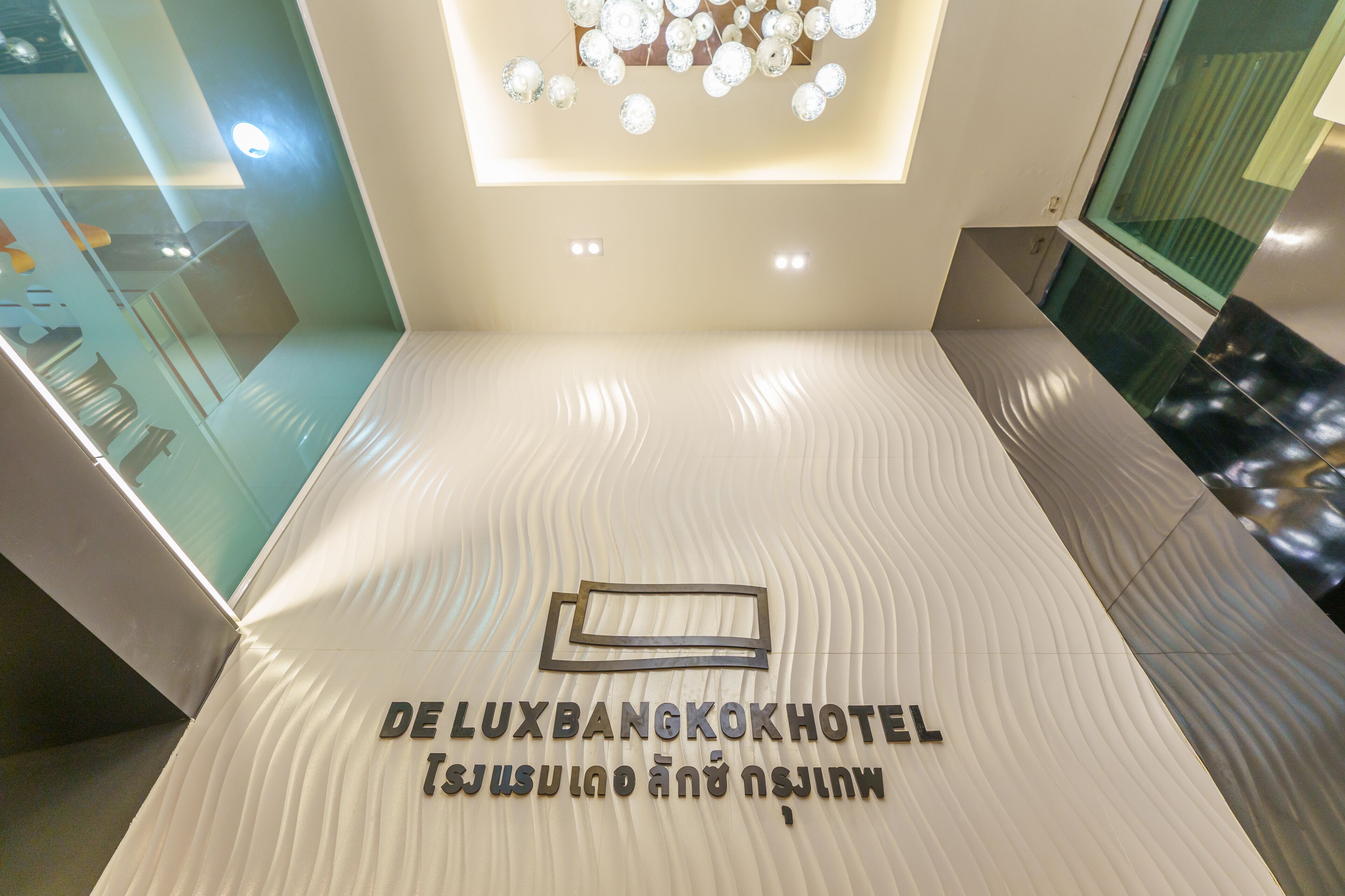 A hotel reception area with a modern design, featuring a textured floor and a ceiling with a decorative light fixture.