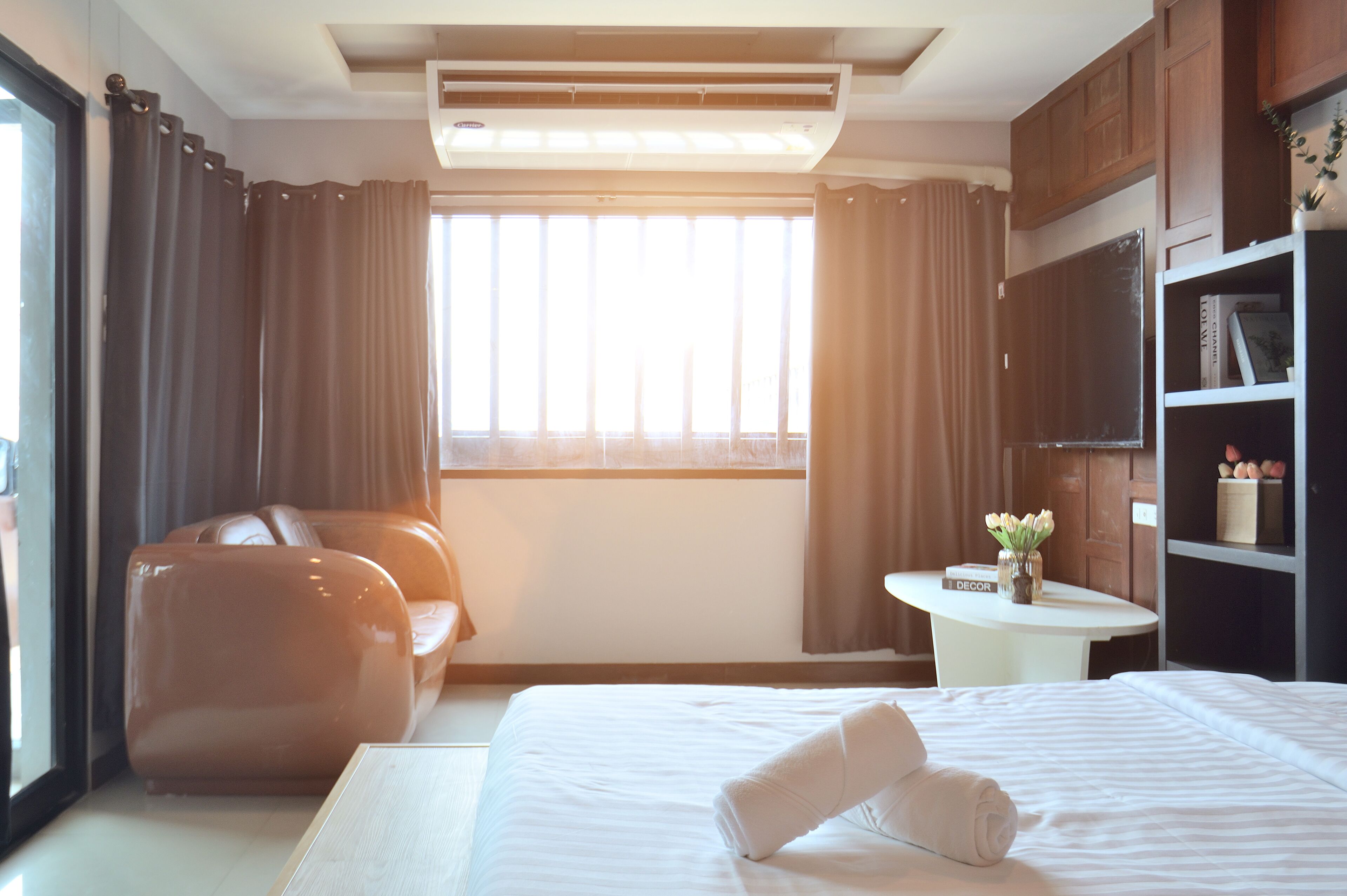 A hotel room with a large bed, a sofa, a small table with a vase, and a bookshelf.