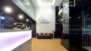A modern hotel reception area with a reception desk, a sofa, and a wall with the hotel's name. - De Lux Bangkok Hotel (Bangkok)