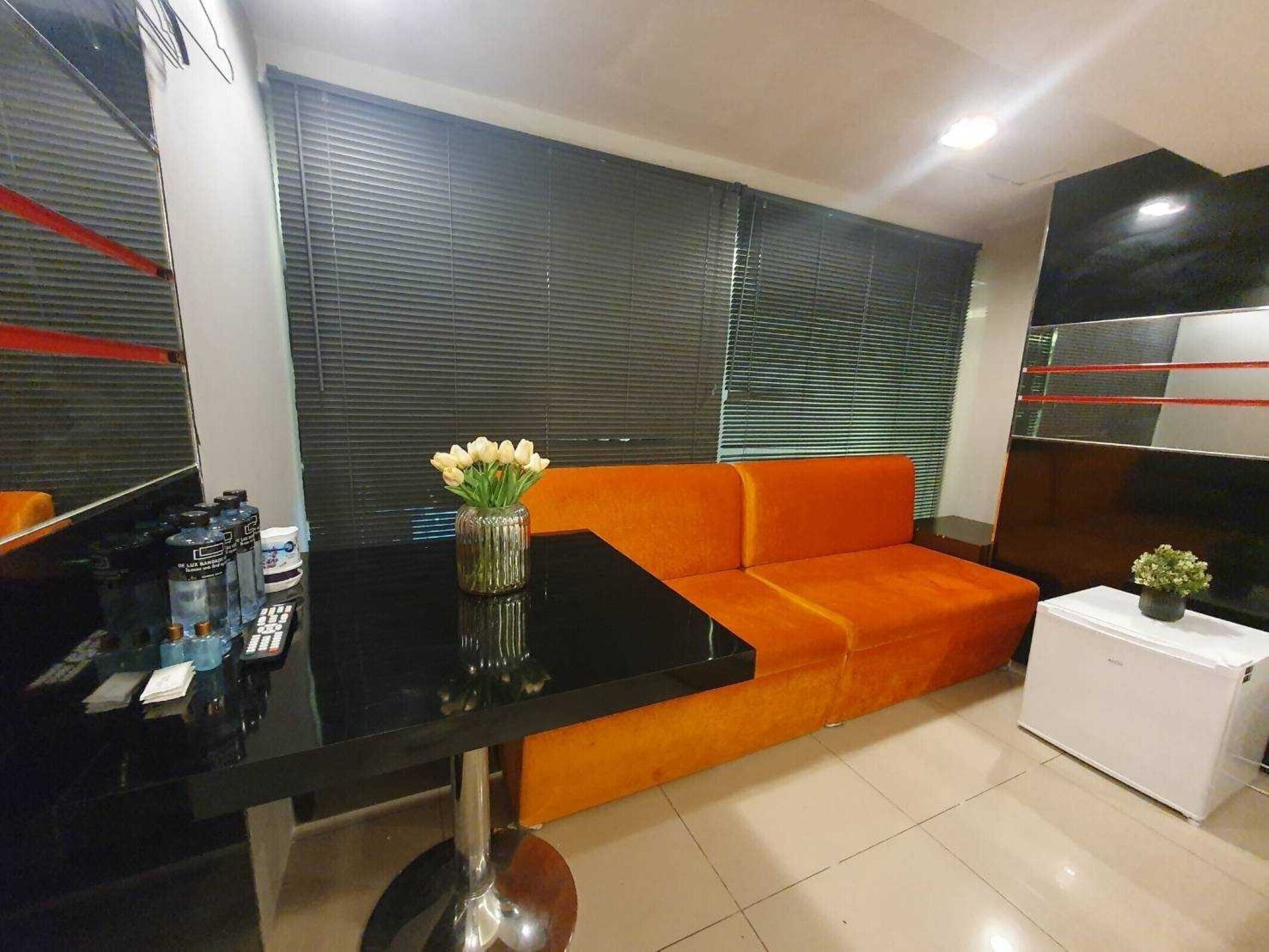 A modern living room with a black glass table, orange sofa, and a small white cabinet.