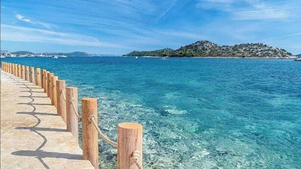 A coastal walkway leading to clear blue waters, a rocky island in the distance, and a clear sky. - Three Apartment Complex With Pool (Tribunj)