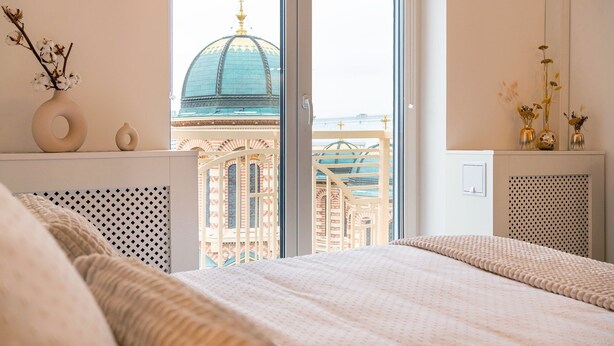 Ein Schlafzimmer mit großem Fenster, einem Bett, einem kleinen Tisch mit einer Vase und einer Heizung.