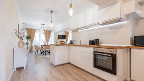 Eine moderne Küche mit weißen Schränken, einer Holz Arbeitsplatte und einem eingebauten Ofen. Im Hintergrund ist eine Essecke mit Tisch und Stühlen zu sehen.