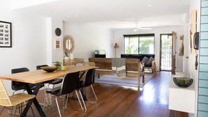 A spacious living area with a wooden dining table, black chairs, a wicker sofa, and a television. - Combi's Cove, Byron beachside oasis - NEW listing specials - Enquire Now. (Suffolk Park)