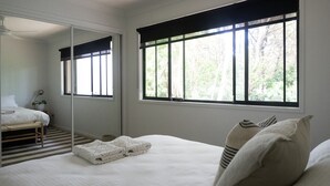 A bedroom with a bed, a large window, a mirror, and a bedside table with a lamp. - Combi's Cove, Byron beachside oasis - NEW listing specials - Enquire Now. (Suffolk Park)