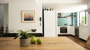 Cozinha moderna com painel de parede verde-água, armários brancos e área de refeições com mesa de madeira e planta em vaso.