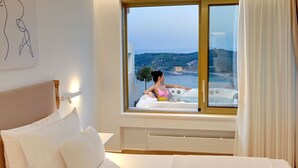 A hotel room with a large window, a bed, and a bathtub.