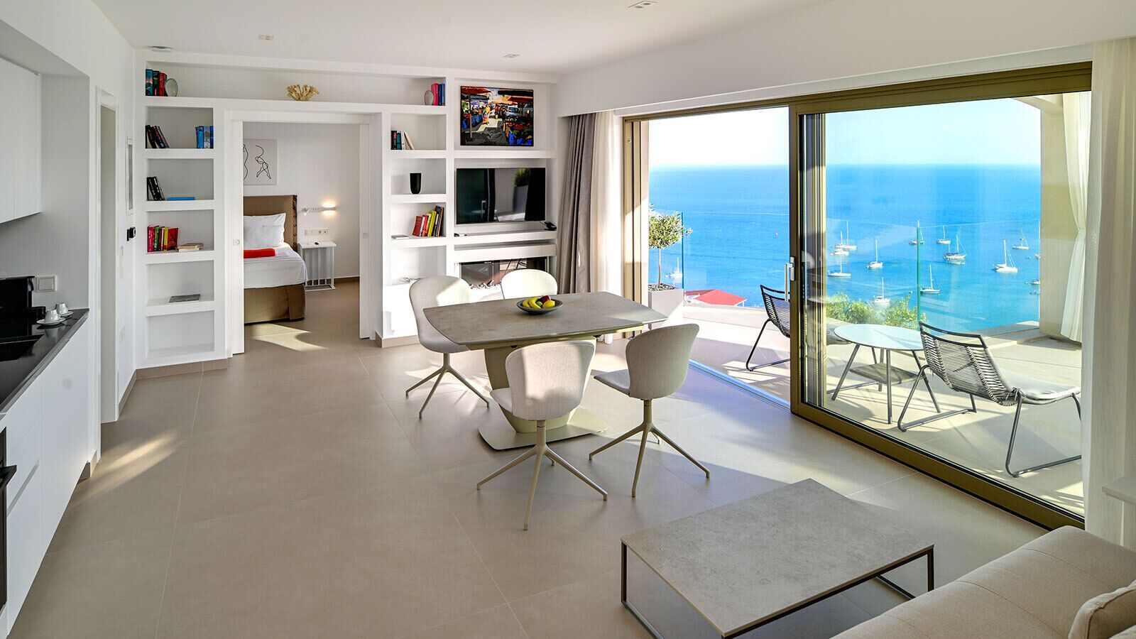 Una sala moderna con comedor, televisor y un gran ventanal corredero que da a un balcón con vista al mar.