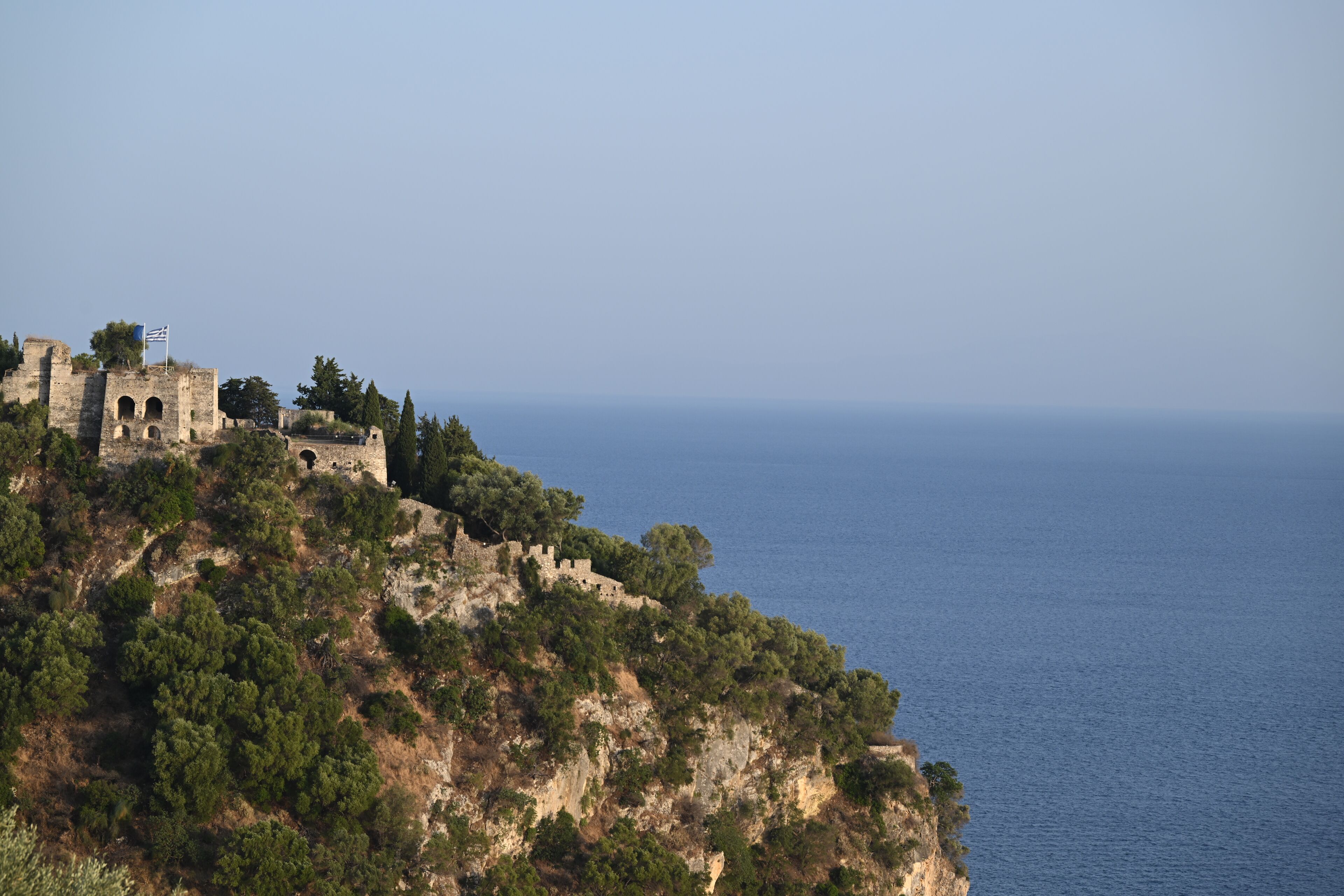 A coastal cliff with ancient ruins and dense greenery.