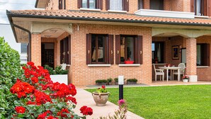 Una casa de dos pisos con fachada de ladrillo, un porche cubierto y un pequeño jardín con flores rojas.