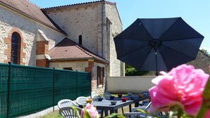 A courtyard with a table and chairs, a large umbrella, and a building with stone walls and a tiled roof. - Quiet and spacious cottage in the countryside (Fourilles)