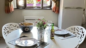 Een eethoek met een witte tafel, witte stoelen, een schaal, een vaas met bloemen, een fles en een magnetron boven de tafel.