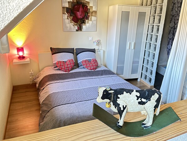 Ein Schlafzimmer mit Bett, Nachttisch mit Lampe, Kleiderschrank und einer dekorativen Skulptur einer Kuh.