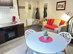 Une cuisine moderne équipée d’un four encastré, d’une machine à café et d’un coin repas avec une table et des chaises blanches.