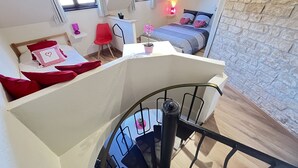 Een slaapkamer in loft-stijl met een schuine kap, een bed met rode en witte beddengoed, een rode stoel, een klein bureau met een lamp en een raam met gordijnen.