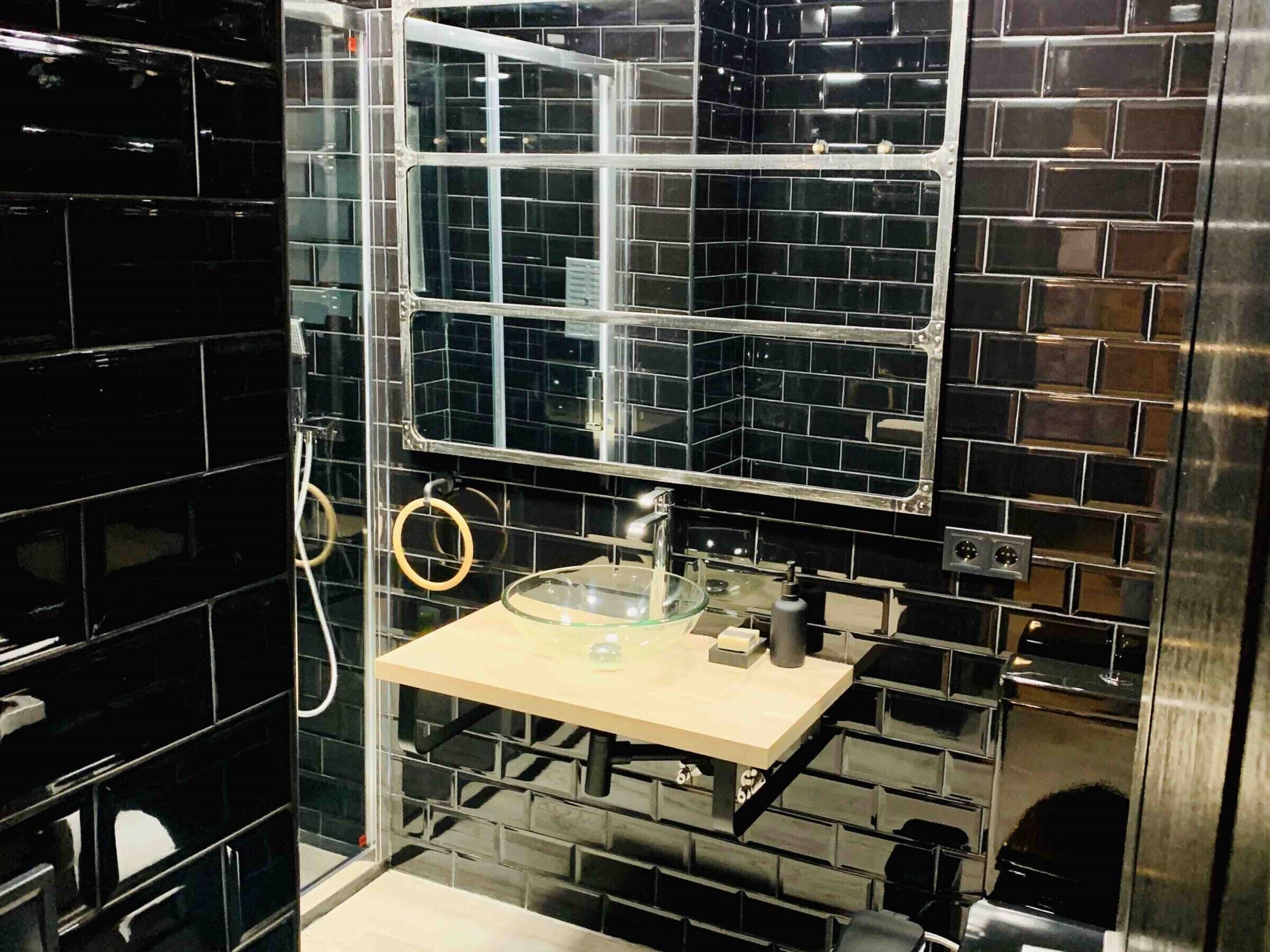 A bathroom with black tiled walls, a glass shower enclosure, and a small sink with a mirror.