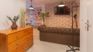 Uma sala de estar com um sofá marrom, cômoda de madeira e uma TV fixada em uma parede com padrão de tijolos.