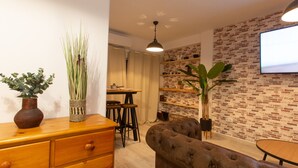 Uma sala de estar moderna com parede em padrão tijolo, cômoda de madeira, sofá estofado e área de jantar com mesa e cadeiras.