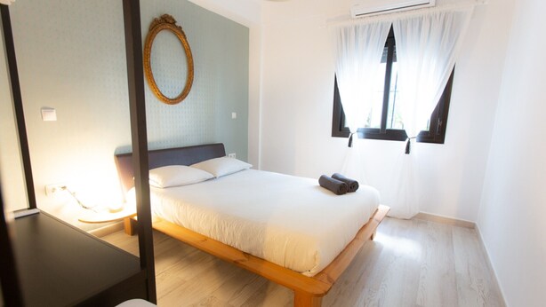 Quarto com cama, mesa de cabeceira, abajur, espelho e ar condicionado.