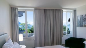 Ein Hotelzimmer mit Bett, einem grünen Sessel, einer Lampe und Meerblick durch große Fenster.