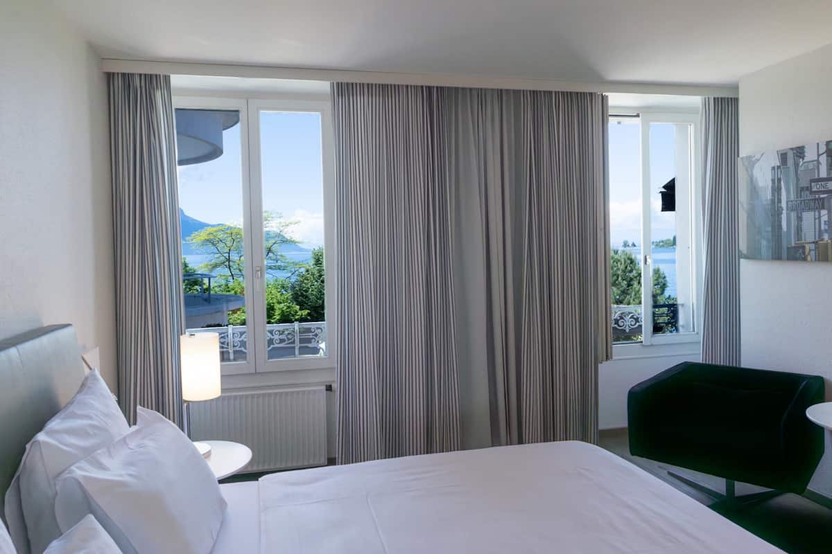 A hotel room with a bed, a green chair, a lamp, and a view of the sea through large windows.