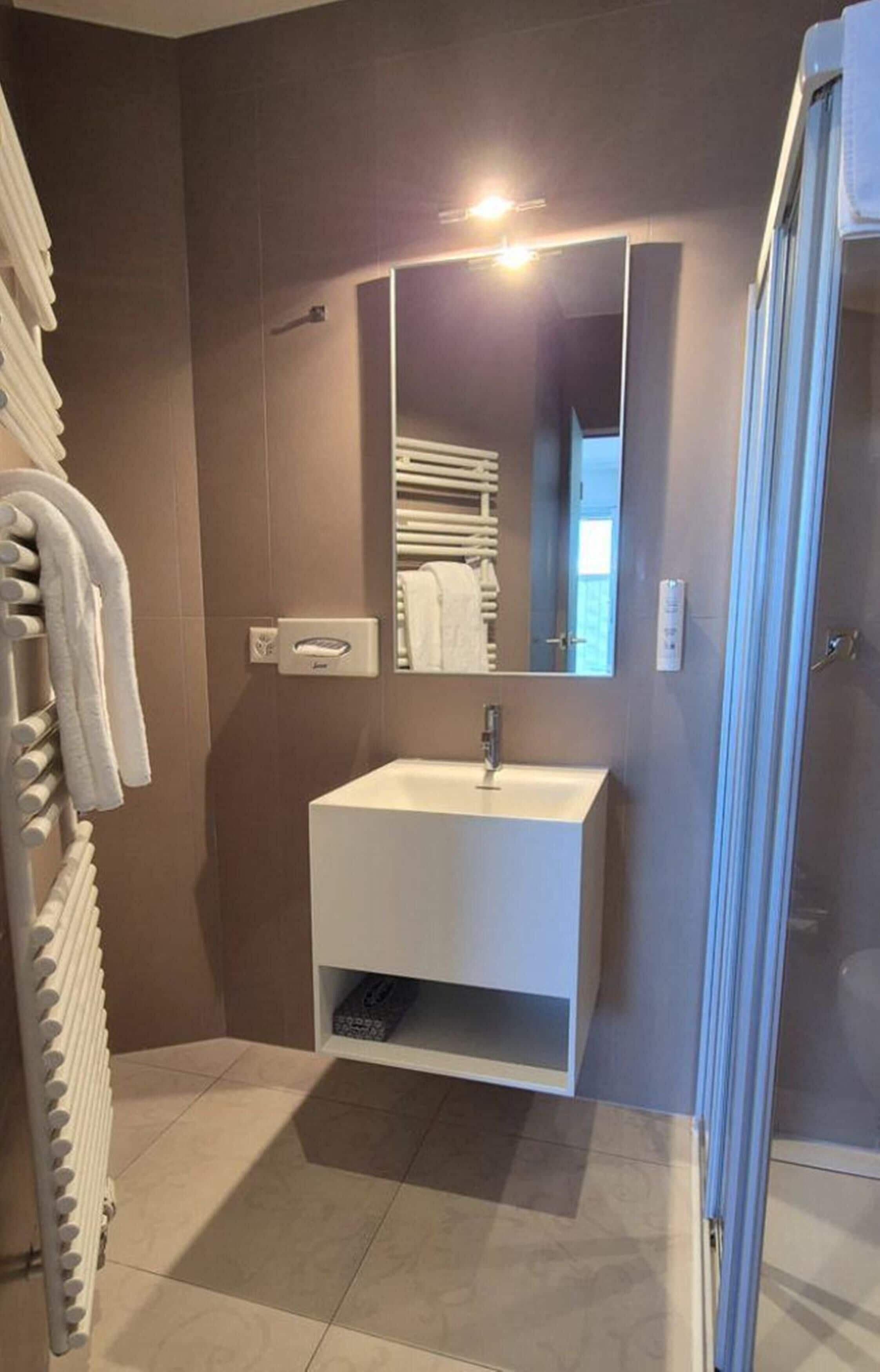 Ein modernes Badezimmer mit einem weißen Waschbecken, einem Spiegel und einem Handtuchhalter.
