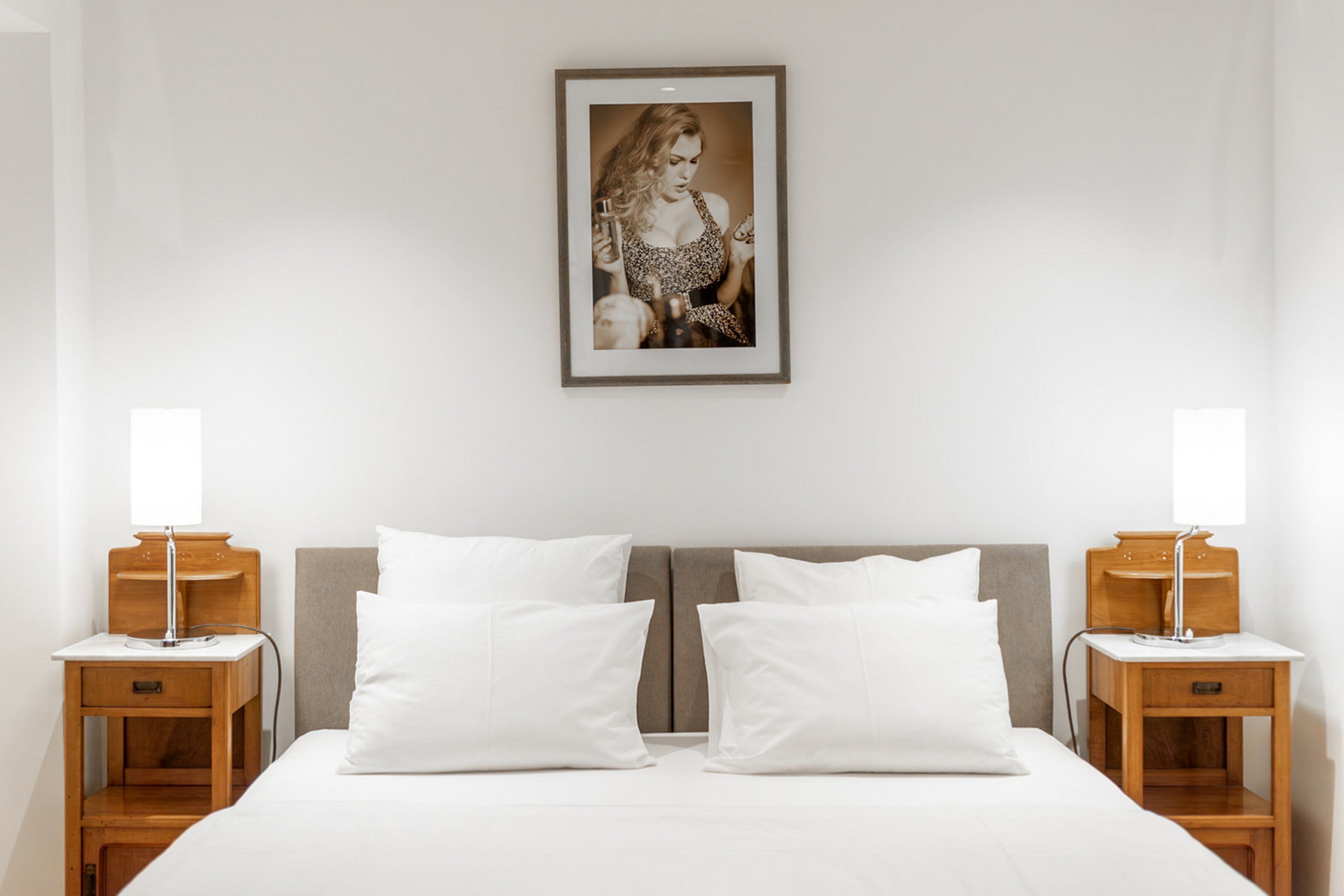 A hotel room with a large bed, two bedside tables with lamps, a framed picture on the wall, and white bedding.