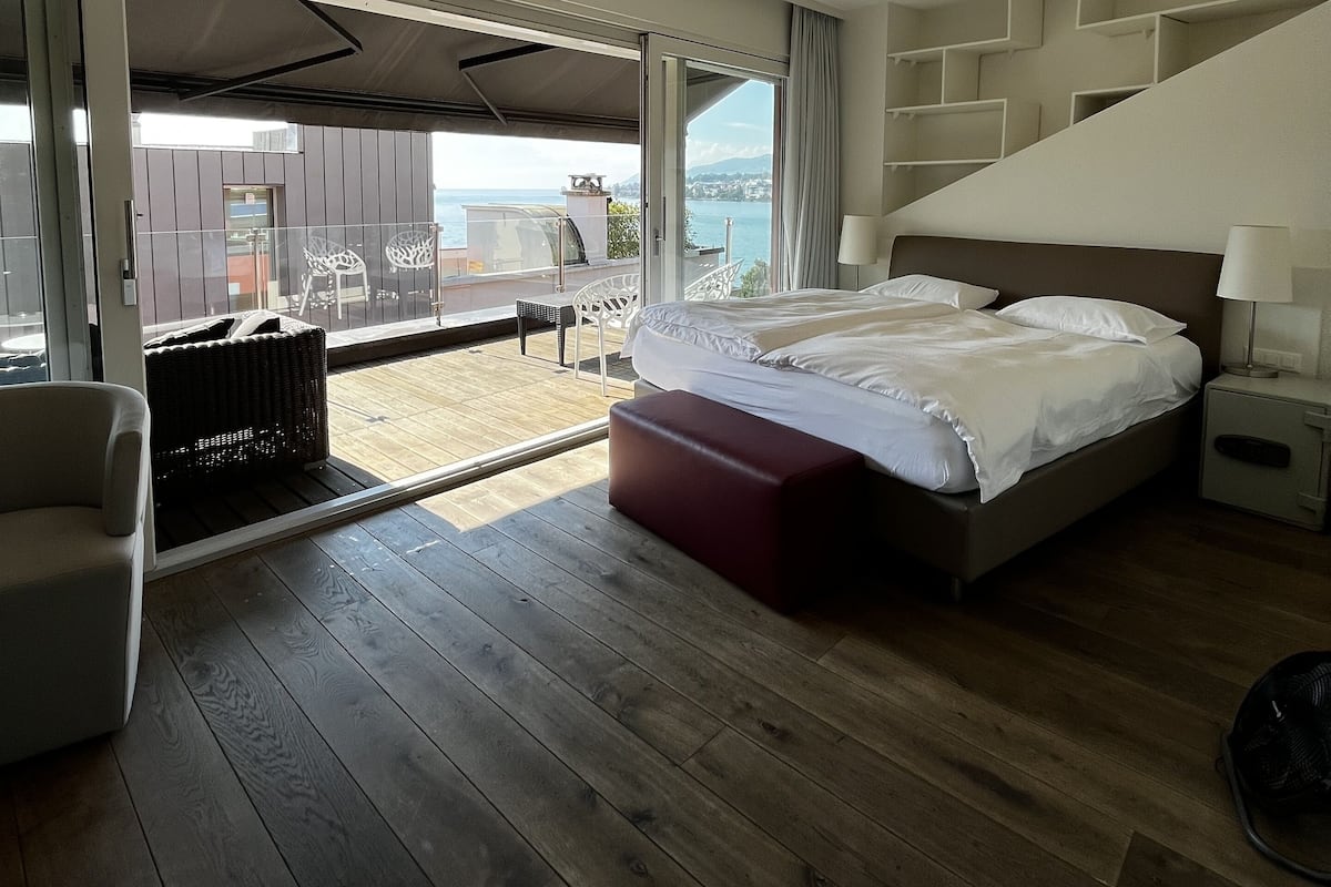 A modern hotel room with a large bed, a seating area with a chair and a table, and a view of the sea.