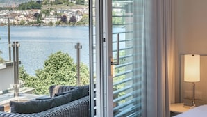 Ein Hotelzimmer mit einer großen Schiebetür, die auf einen Balkon mit Blick auf einen See und entfernte Gebäude führt.