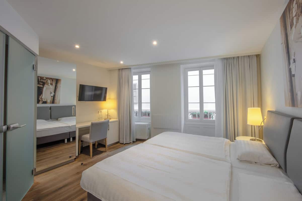 A hotel room with a large bed, a desk, a chair, a TV, and a window with curtains.