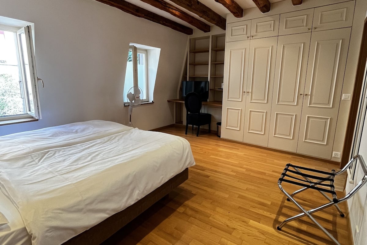 A bedroom with a bed, wooden beams, a desk, a chair, and a wardrobe.