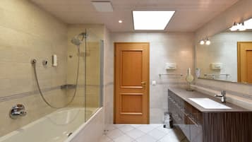 A modern bathroom with a glass-enclosed shower, a wooden door, a vanity with a mirror, and a large window above the sink.