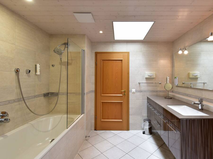 Un bagno moderno con doccia vetrata, una porta in legno, un mobile lavabo con specchio e un'ampia finestra sopra il lavandino.