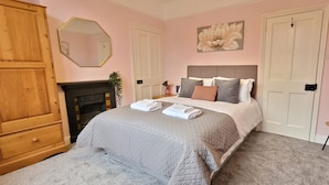 A bedroom with a bed, a wooden wardrobe, a mirror, a fireplace, and a flower painting on the wall. - 2 Bed Holiday Home with on-street parking and river walks (York)