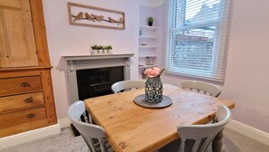 A dining area with a wooden table, white chairs, a fireplace, and a window with blinds. - 2 Bed Holiday Home with on-street parking and river walks (York)