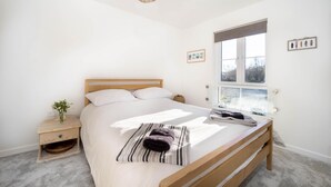 A bedroom with a wooden bed, a bedside table, a window with a view, and a hanging light fixture.