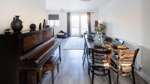 A dining area with a piano, wooden chairs, a table set for four, and a view of the outdoors through a glass door.