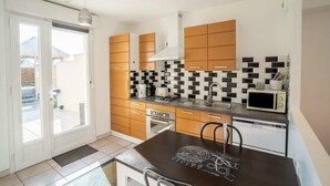 A modern kitchen with wooden cabinets, a black and white tiled backsplash, a microwave, and a dining area with a table and chairs. - House facing the sea, with swimming pool and SPA
OMAHA GITES (Vierville-sur-Mer)