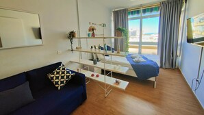 Ein modernes Zimmer mit einer Couch, einem Bett mit Blick, einem Fernseher und einem Pflanzenregal.