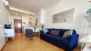 Ein modernes Wohnzimmer mit einem blauen Sofa, einem Essbereich mit Stühlen und einer Küche im Hintergrund.
