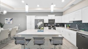 Una cocina moderna con armarios blancos, una isla grande con taburetes de bar, electrodomésticos de acero inoxidable e iluminación colgante.