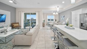 Una cocina moderna con una isla central, comedor con sillas y sala de estar con sofá y televisor.