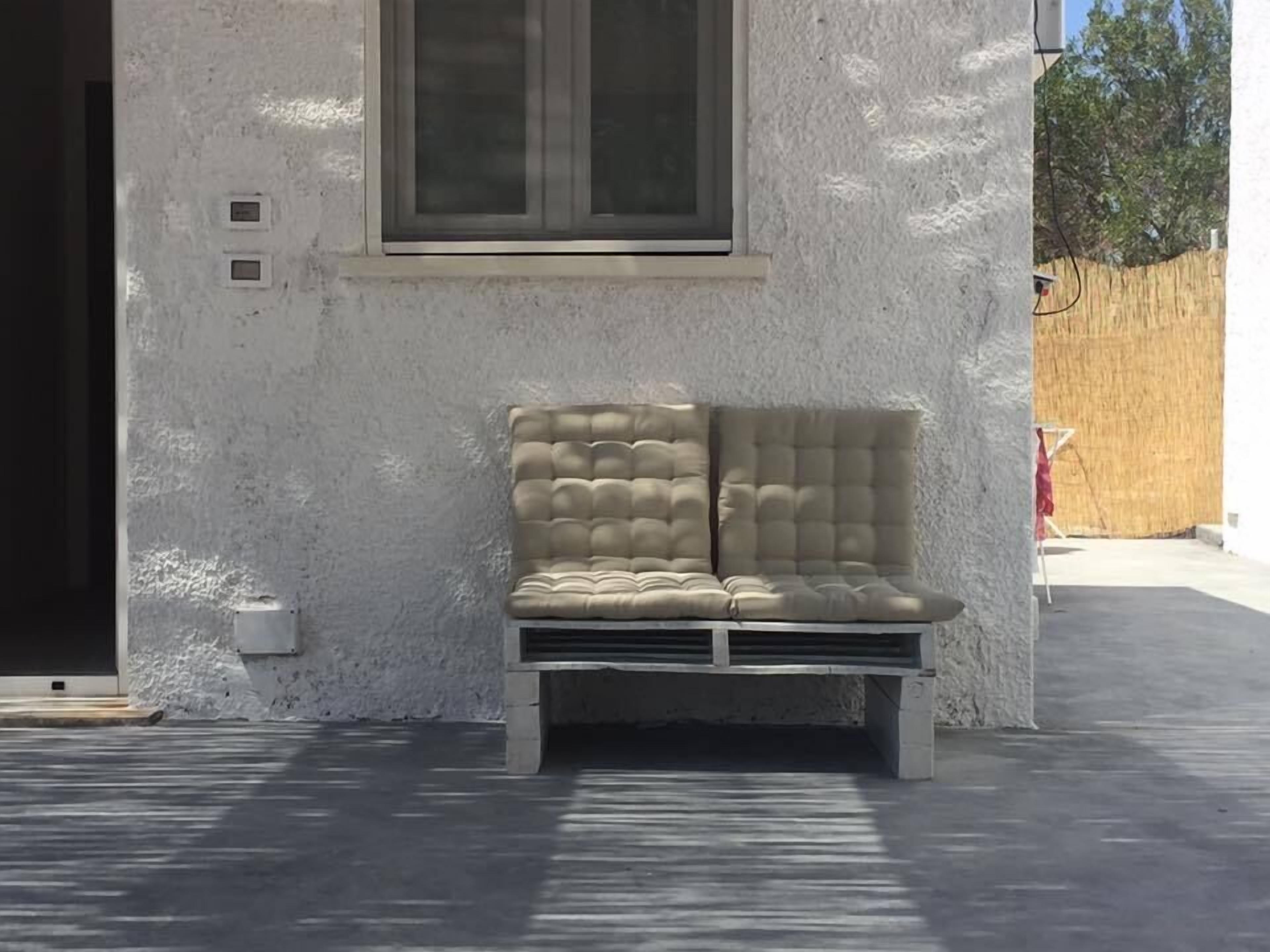 A beige cushioned bench against a textured wall with a window above it.