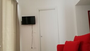 A room with a white door, a mounted flat-screen TV, and a red sofa. - Stella del Sud Guesthouse  (Patu)