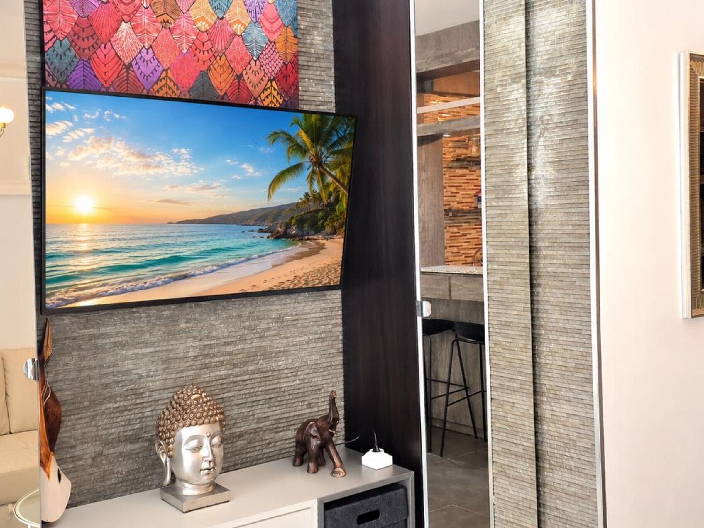 A room with a large TV displaying a beach scene, a Buddha statue, and a small elephant figurine on a white console.