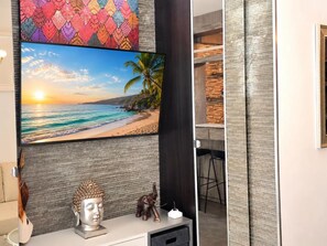 A room with a large TV displaying a beach scene, a Buddha statue, and a small elephant figurine on a white console. - Modern Apartment with Terrace, Near Beaches & Train Station, Fully Equipped (Torremolinos)